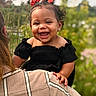 Hannah is registered to the contest to win money with this photo: child, toddler, smiling, happy, red_bows, curly_hair, black_dress, earrings, adult, plaid_shirt, outdoor, nature, greenery, portrait, daylight, person, holding, cute, joyful, baby