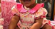 Hannah joined the competition — help win amazing prizes! baby, child, smiling, pink_dress, bow, curly_hair, milestone_plaque, birthday, gift_wrap, celebration, sitting, indoors, happy, cute, person, infant, face, hands, feet, decorations