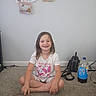 Alyssa is registered to the contest to win money with this photo: child, girl, smile, missing_teeth, sitting, carpet, floor, backpack, soda_bottle, wall, drawing, artwork, casual, home, indoor, happy, tshirt, shorts, hair, person