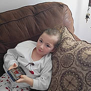 Alyssa joined the competition — help win amazing prizes! child, pajamas, cherry_pattern, smartphone, cartoon, couch, leather, pillow, indoor, relaxed, casual, person, young_child, home, technology, screen, seated, comfort, white_shirt, brown