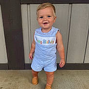 Beckett is registered to the contest to win money with this photo: toddler, child, standing, romper, happy_birthday, blonde_hair, blue_eyes, smiling, footwear, loafers, concrete_floor, wooden_wall, outdoor, casual_clothing, cute, portrait, young_child, fashion, one_year_old, celebration