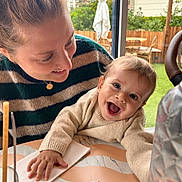 Louis a rejoint le concours — aidez-le/la à gagner de superbes lots ! baby, woman, smile, happy, table, window, indoor, clothing, striped_sweater, napkin, hand, face, person, glass, chair, greenery, background, daylight, portrait, family