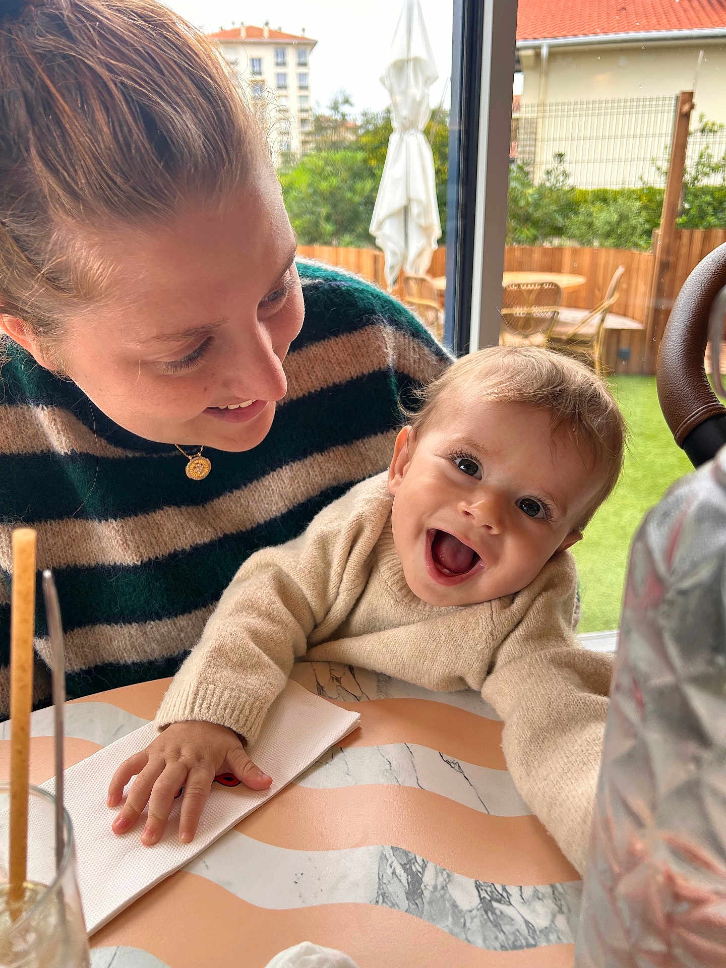 Louis a rejoint le concours — aidez-le/la à gagner de superbes lots ! baby, woman, smile, happy, table, window, indoor, clothing, striped_sweater, napkin, hand, face, person, glass, chair, greenery, background, daylight, portrait, family