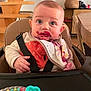 Gabriel a rejoint le concours — aidez-le/la à gagner de superbes lots ! baby, high_chair, bib, messy_face, toy, indoor, wooden_furniture, curious_expression, child, feeding_time, colorful_toy, smudged_food, casual_clothing, infant, wooden_stairs, home_interior, seat_belt, table, closeup, person