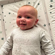 Zoe is registered to the contest to win money with this photo: baby, smiling, infant, ribbed_sweater, changing_mat, star_pattern, happy, face, person, child, cute, skin, head, cheek, indoors, young, portrait, clothing, lying_down, bright_eyes