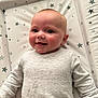 baby, smiling, infant, ribbed_sweater, changing_mat, star_pattern, happy, face, person, child, cute, skin, head, cheek, indoors, young, portrait, clothing, lying_down, bright_eyes
