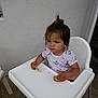 cartoon_print, child, cute, expression, floor, floral_pattern, food, hair_clip, high_chair, indoor, person, seat, shirt, small, snack, table, toddler, wall, white, young