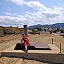 Ryan participe au concours pour gagner de l'argent avec cette photo : boy, child, red_clothing, outdoor, sculpture, concrete_platform, peace_sign, wooden_post, smiling_face, rocks, hill, clouds, sky, houses, mountains, sunlight, casual, sand, path, summer