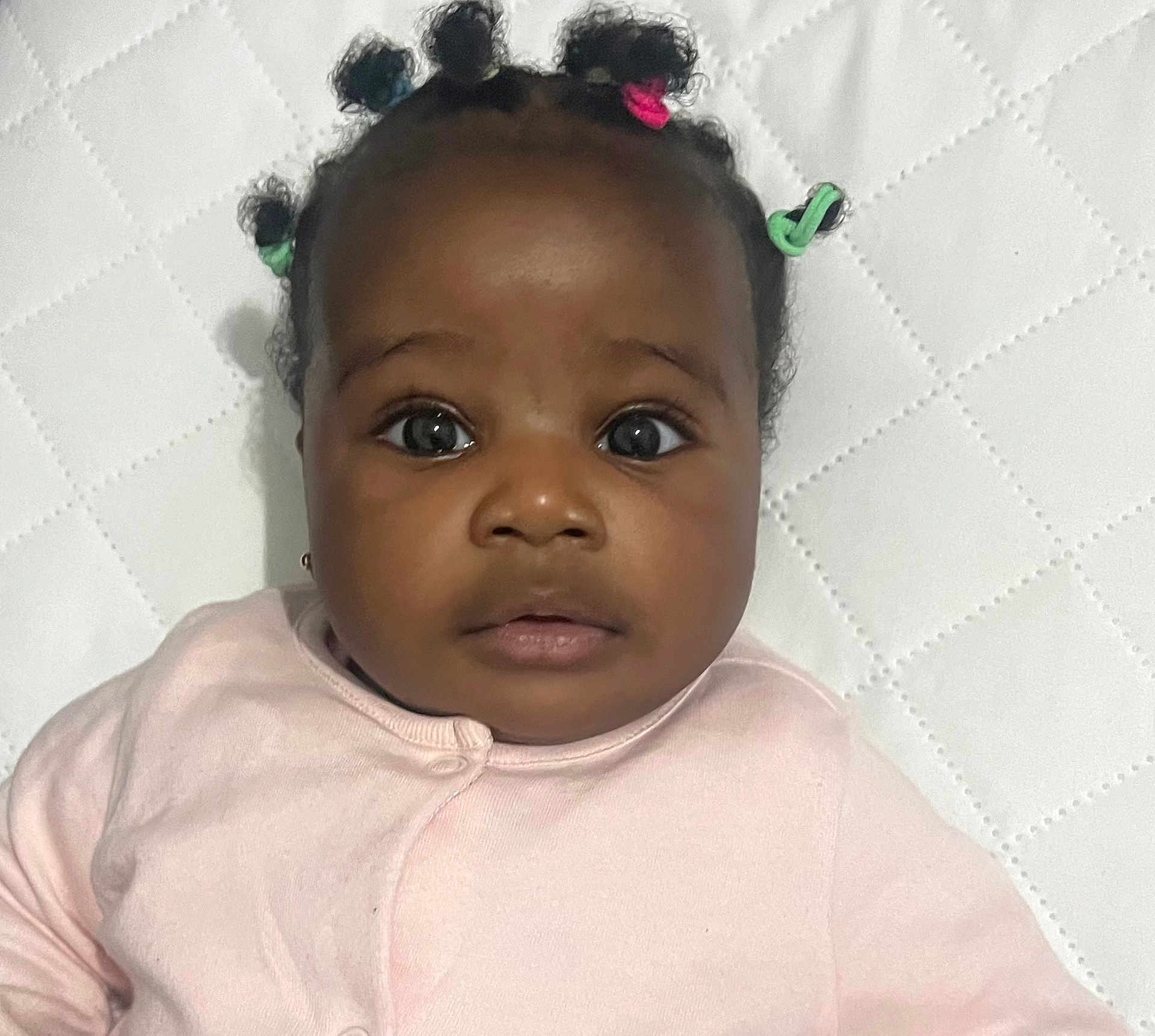 Mirabel joined the competition — help win amazing prizes! baby, infant, child, face, eyes, hair, hair_ties, pink_clothing, quilted_background, portrait, cute, closeup, skin, person, young_child, expression, indoors, head, looking, lying_down