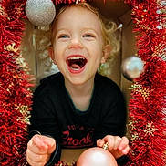 Malo participe au concours pour gagner de l'argent avec cette photo : toddler, child, smiling, happy, curly_hair, christmas, ornament, holiday, festive, red_tinsel, decoration, gold_snowflakes, indoors, joyful, portrait, cute, holding, celebration, fun, face