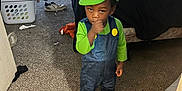 Zian joined the competition — help win amazing prizes! child, costume, luigi_hat, blue_overalls, green_shirt, indoor, carpet, bedroom, bed, laundry_basket, clothes, shoe, carpet_floor, person, toddler, standing, thinking, thumb_in_mouth, cute, casual