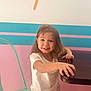 Delilah is registered to the contest to win money with this photo: bright, casual_clothing, chair, child, colorful, cute, furniture, happy, indoor, long_hair, pastel_wall, person, pink_pants, playful, portrait, room, smiling, table, white_shirt, young