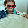 child, girl, sunglasses, heart_shaped, braids, pajamas, indoor, portrait, face, hand, table, colorful, cute, young, looking_down, wearing, eyewear, fashion, closeup, soft_light