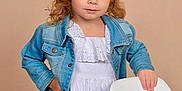 Delilah is registered to the contest to win money with this photo: casual_clothing, chair, child, curly_hair, cute, denim_jacket, fashion, girl, hand_on_hip, indoor, light_skin, long_sleeves, neutral_background, portrait, posing, smile, standing, studio, white_dress, young_child