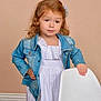 casual_clothing, chair, child, curly_hair, cute, denim_jacket, fashion, girl, hand_on_hip, indoor, light_skin, long_sleeves, neutral_background, portrait, posing, smile, standing, studio, white_dress, young_child