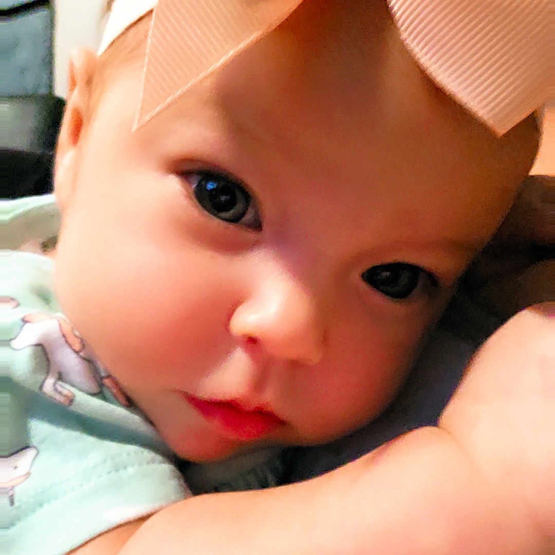Penelopy is registered to the contest to win money with this photo: baby, infant, child, portrait, close_up, face, eyes, bow, hair_accessory, peach, smiling, curious, indoors, clothing, pastel, warm_lighting, arm, sitting, cuddling, photography