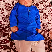 Shahzain joined the competition — help win amazing prizes! baby, child, blue_clothing, traditional_outfit, bedspread, patterned_fabric, indoor, lying_down, footwear, curious_expression, face, hands, pajamas, brown_pattern, white_pants, young_child, portrait, cute, indoors, resting