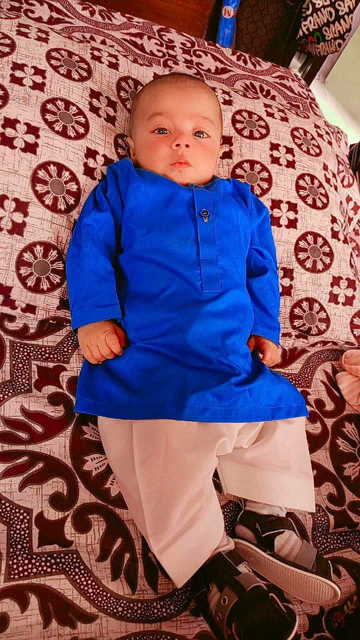 Shahzain joined the competition — help win amazing prizes! baby, child, blue_clothing, traditional_outfit, bedspread, patterned_fabric, indoor, lying_down, footwear, curious_expression, face, hands, pajamas, brown_pattern, white_pants, young_child, portrait, cute, indoors, resting