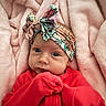 baby, infant, headband, red_clothing, blanket, soft_texture, cute, portrait, child, newborn, face, hands, lying_down, colorful, floral_pattern, cozy, warm, pink, closeup, expression