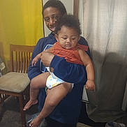 Alina is registered to the contest to win money with this photo: adult, baby, child, diaper, orange_clothing, holding, smiling, indoor, curtain, chair, carpet, socks, shoes, person, family, happy, toddler, furniture, wall, portrait
