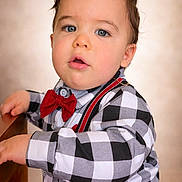 Asher is registered to the contest to win money with this photo: toddler, child, boy, face, blue_eyes, curly_hair, red_bow_tie, suspenders, checkered_shirt, long_sleeve, portrait, indoor, wooden_surface, curious_expression, close_up, fashion, cute, young_child, casual_clothing, soft_background