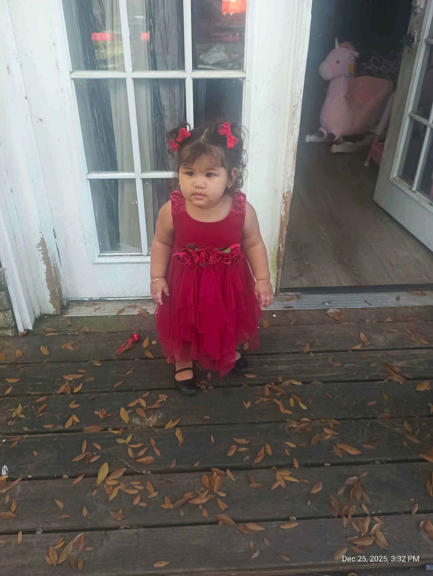 Jaylani is registered to the contest to win money with this photo: toddler, child, girl, red_dress, curly_hair, hair_bows, porch, wooden_floor, dry_leaves, door, glass_panels, stuffed_unicorn, toy, indoor, outdoor, footwear, black_shoes, bracelet, window, home