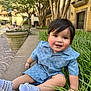 toddler, child, boy, smiling, blue_clothing, white_sneakers, grass, sidewalk, urban, trees, potted_plant, brick_building, outdoor, daylight, face, happy, sitting, cute, short_hair, casual