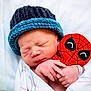 Miles is registered to the contest to win money with this photo: newborn, baby, infant, sleeping, hat, knitted_hat, plush_toy, red_toy, superhero_toy, wrapped, blanket, bed, closeup, cozy, cute, soft_light, hand, peaceful, portrait, human