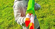 Alfie is registered to the contest to win money with this photo: casual_clothing, child, daylight, fence, fun, garden, grass, green_grass, greenery, hoodie, nature, outdoor, person, playful, red_shoes, smiling, sunny, toy_gun, water_gun, young_boy