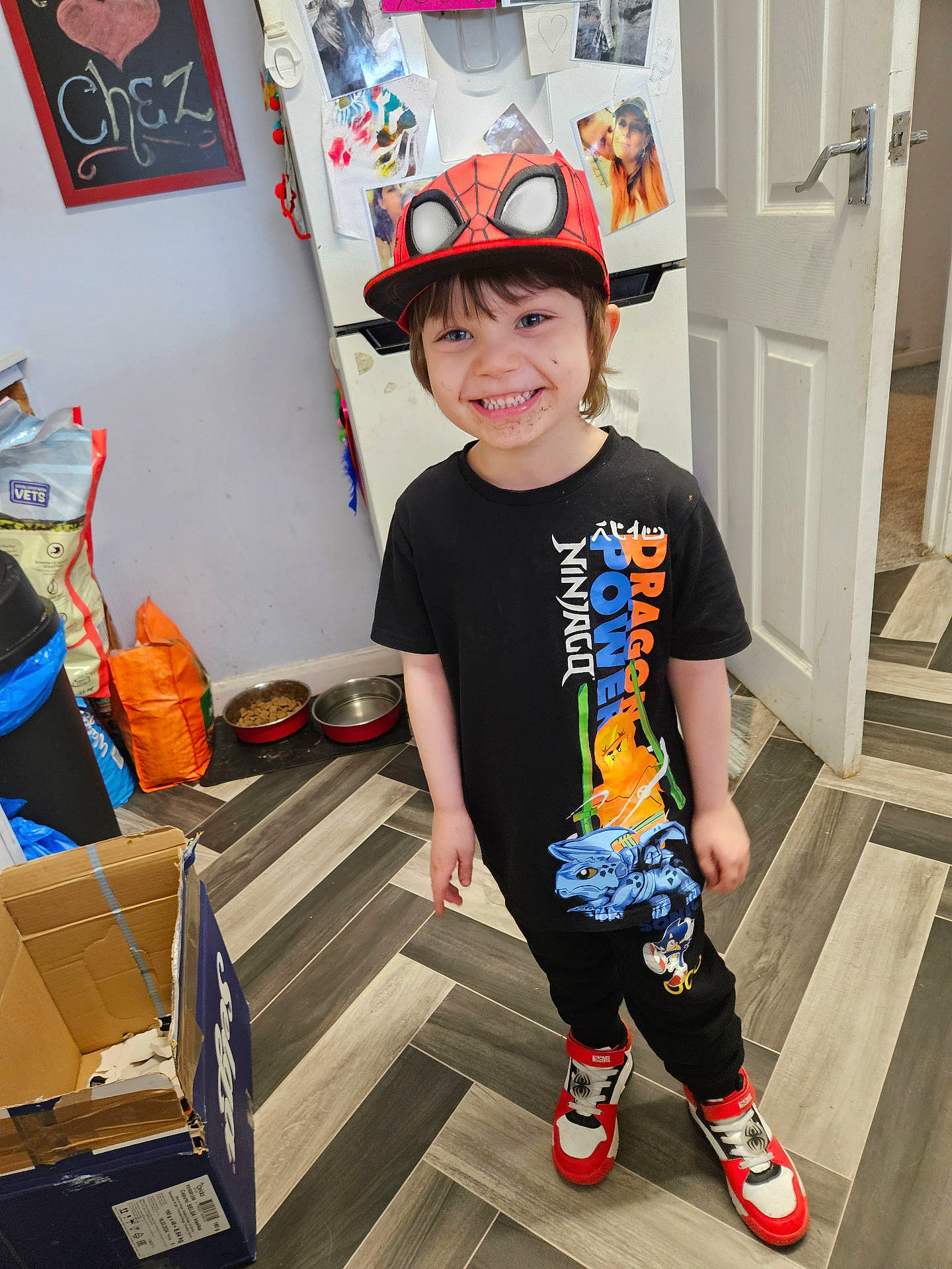 Alfie is registered to the contest to win money with this photo: boy, cap, cardboard_box, chalkboard, child, door, dragon_power, floor, happy, kitchen, ninjago, pet_food, photography, red_shoes, refrigerator, shoes, smiling, spiderman, standing, tshirt