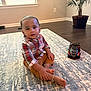 toddler, child, indoor, carpet, toy_car, plaid_shirt, pants, barefoot, bracelets, floor, plant, window, light, living_room, person, furniture, wood_floor, curious, sitting, home
