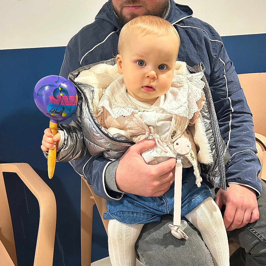 Juna a rejoint le concours — aidez-le/la à gagner de superbes lots ! baby, cap, child, clothing, curious, expression, floor, footwear, holding, indoor, jacket, man, person, plastic_chair, rattle, seated, sitting, toy, wall, wood