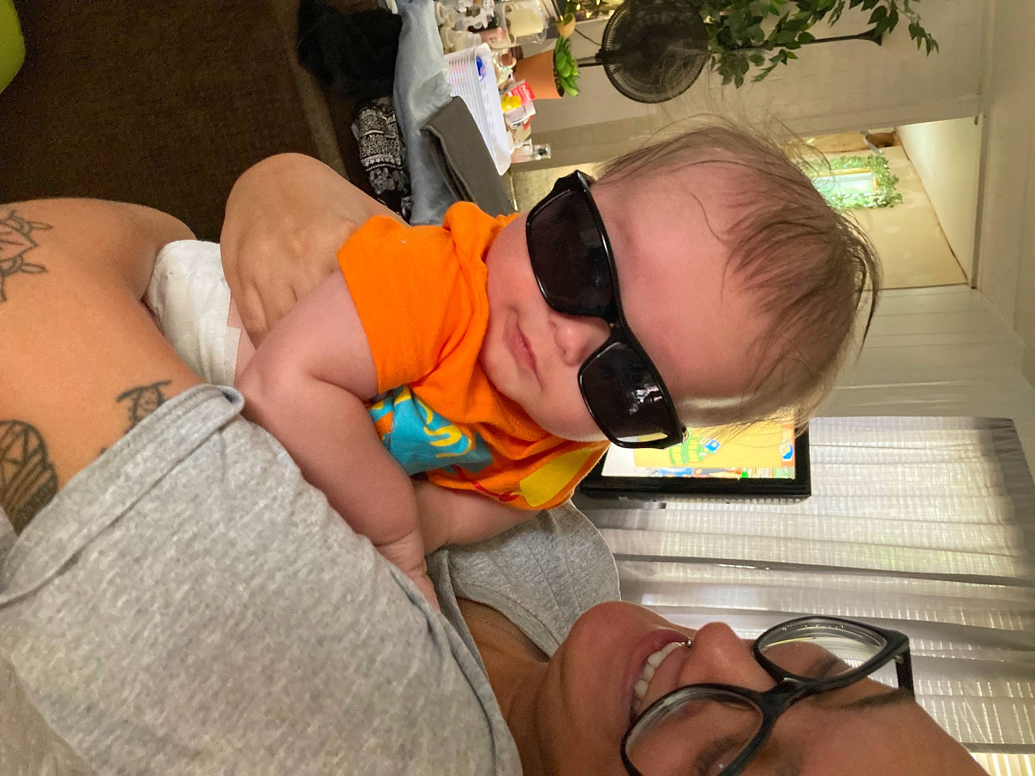 Hero is registered to the contest to win money with this photo: arm, baby, child, comfort, eyewear, finger, glasses, hairstyle, hand, human_body, human_leg, joy, knee, leg, mouth, organ, person, plant, sitting, thigh
