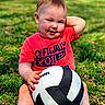 Clyde is registered to the contest to win money with this photo: toddler, child, grass, volleyball, red_shirt, sitting, smiling, outdoor, playful, hand_behind_head, cute, sunlight, shoes, yellow_socks, portrait, baby, happy, nature, person, sport