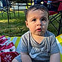 toddler, child, outdoor, grass, blanket, striped_mat, nike_shirt, curious_expression, folding_chair, sunlight, short_hair, sitting, person, daytime, casual_clothing, greenery, summer, face, eyes, mouth