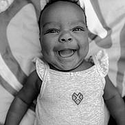 Amiah is registered to the contest to win money with this photo: baby, smiling, face, infant, clothing, sleeveless_top, patterned_blanket, black_and_white, cute, happy, portrait, lying_down, child, skin, head, eyes, mouth, person, small_child, joyful