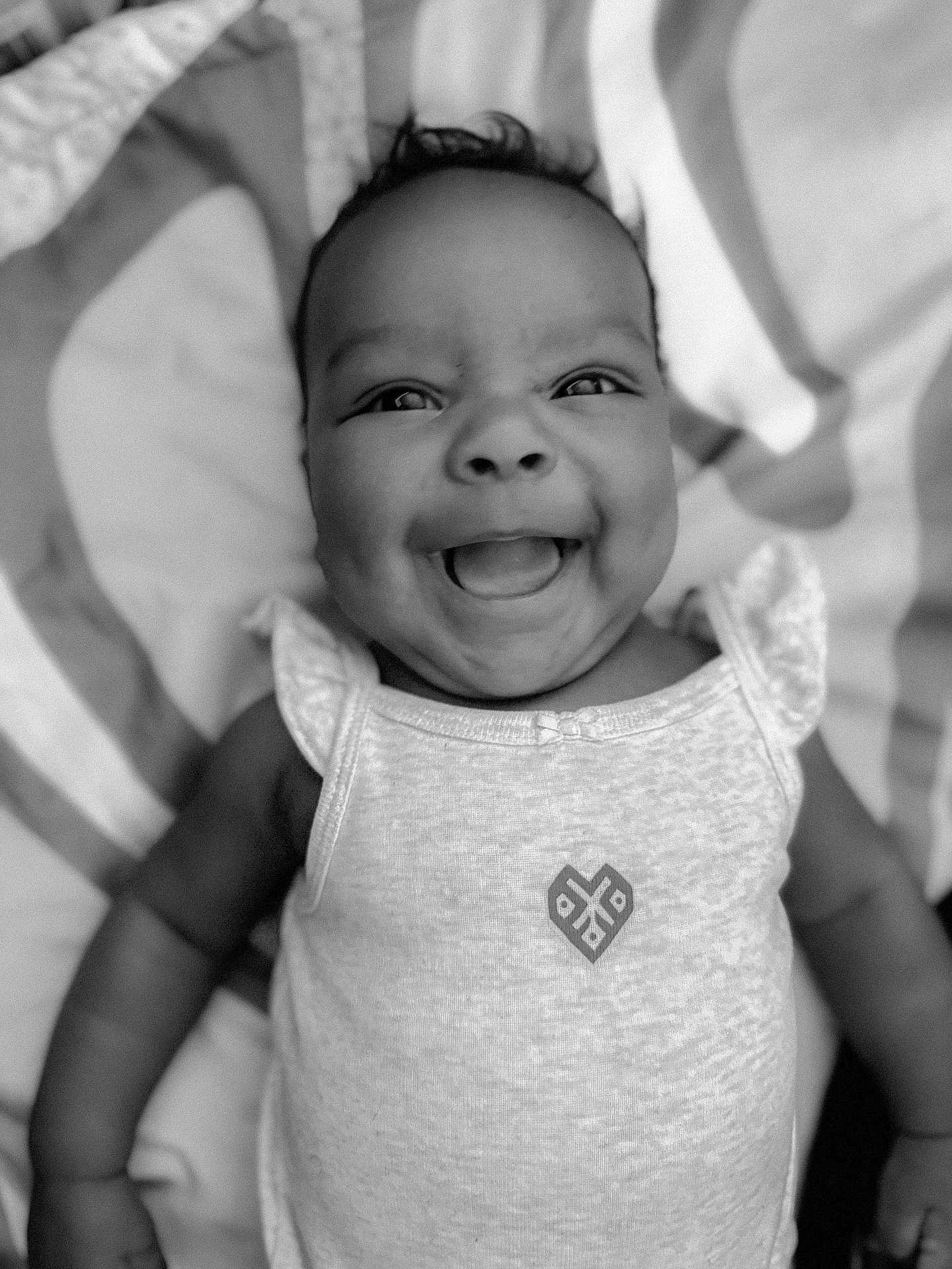 Amiah is registered to the contest to win money with this photo: baby, smiling, face, infant, clothing, sleeveless_top, patterned_blanket, black_and_white, cute, happy, portrait, lying_down, child, skin, head, eyes, mouth, person, small_child, joyful