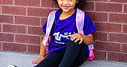 Zai'Lynn joined the competition — help win amazing prizes! black_leggings, black_shoes, brick_wall, casual_clothing, child, concrete_floor, curly_hair, cute, daylight, fashion, happy, outdoor, person, pink_backpack, portrait, purple_shirt, resting, sitting, smile, young_girl