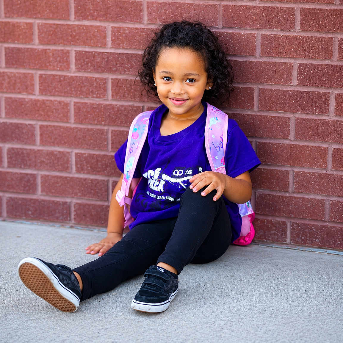 Zai'Lynn joined the competition — help win amazing prizes! child, sitting, brick_wall, purple_shirt, pink_backpack, curly_hair, smile, black_shoes, black_leggings, outdoor, concrete_floor, casual_clothing, young_girl, portrait, daylight, happy, resting, fashion, person, cute