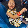 Zai'Lynn is registered to the contest to win money with this photo: arcade, arcade_game, blue_seat, bracelet, child, entertainment, face_stickers, fun, game_machine, girl, happy, indoor, playing, racing_game, seat, smiling, steering_wheel, sunflower_dress, white_bow, wristband