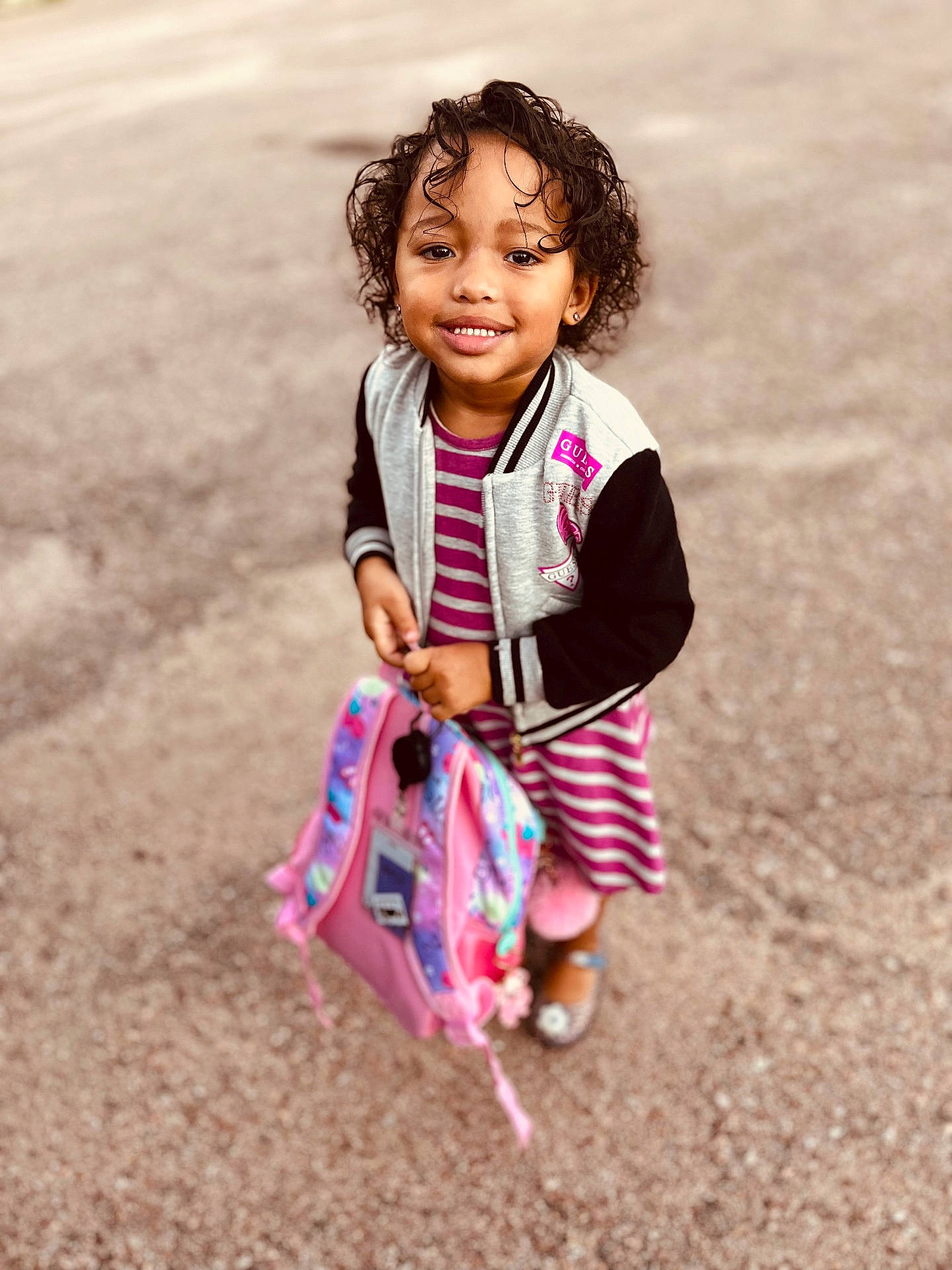 Zai'Lynn is registered to the contest to win money with this photo: backpack, casual, child, curly_hair, cute, fashion, feet, girl, happy, jacket, outdoor, pavement, person, pink, portrait, shoes, smiling, standing, striped_dress, young