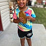 Zai'Lynn joined the competition — help win amazing prizes! child, smiling, curly_hair, colorful_shirt, shorts, sneakers, wooden_box, outdoor, concrete, house, yard, daylight, happy, portrait, standing, person, casual_clothing, playful, front_view, young_kid