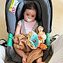 baby, blanket, car_seat, child, clothing, cute, face, floor, footwear, head, indoor, infant, pacifier, person, plush_toy, seat_belt, sitting, sneakers, toy, young_child