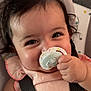 adorable, baby, black_straps, car_seat, child, close_up, curly_hair, cute, face, hand, happy, indoors, infant, pacifier, person, pink_clothing, portrait, smiling, soft_lighting, young
