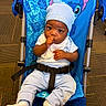 baby, child, infant, stroller, sitting, portrait, face, eyes, thumb_sucking, hat, beanie, white_clothing, blue, harness, carpet, indoor, smiling, baby_fashion, stitch, travel