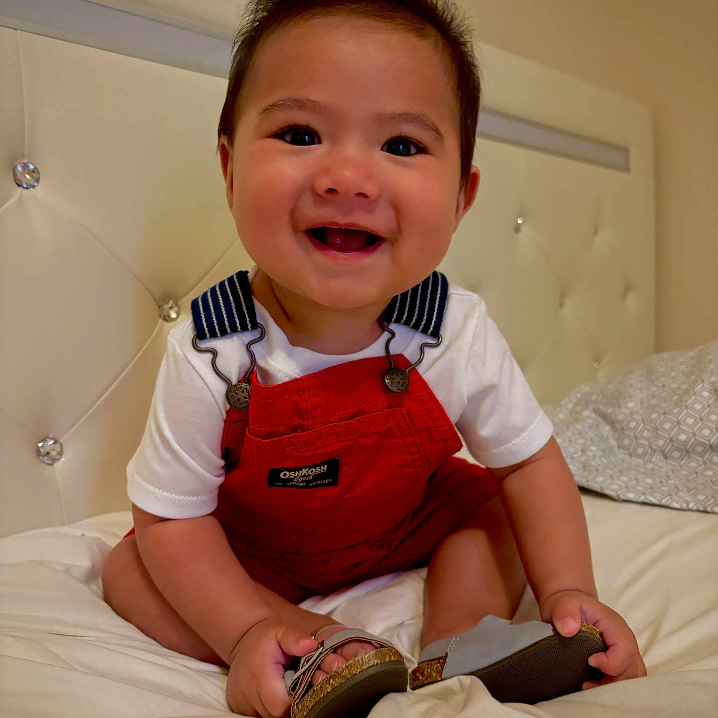 Duane Ray Jaramillo joined the competition — help win amazing prizes! baby, bed, bedding, child, clothing, cute, face, feet, hands, happy, headboard, indoor, infant, person, portrait, red_overalls, sandals, sitting, smiling, white_shirt
