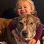 affection, blanket, blond_hair, brown_dog, child, closeup, couch, cozy, dog, domestic_animal, friendship, happy, hugging, indoor, pet, portrait, smiling, spot_pattern, warmth, young_child