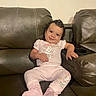 Adrianna is registered to the contest to win money with this photo: baby, child, infant, smiling, happy, portrait, sitting, couch, leather, living_room, indoor, clothing, pink_outfit, cartoon, minnie_mouse, baby_booties, dark_hair, face, furniture, family_photo