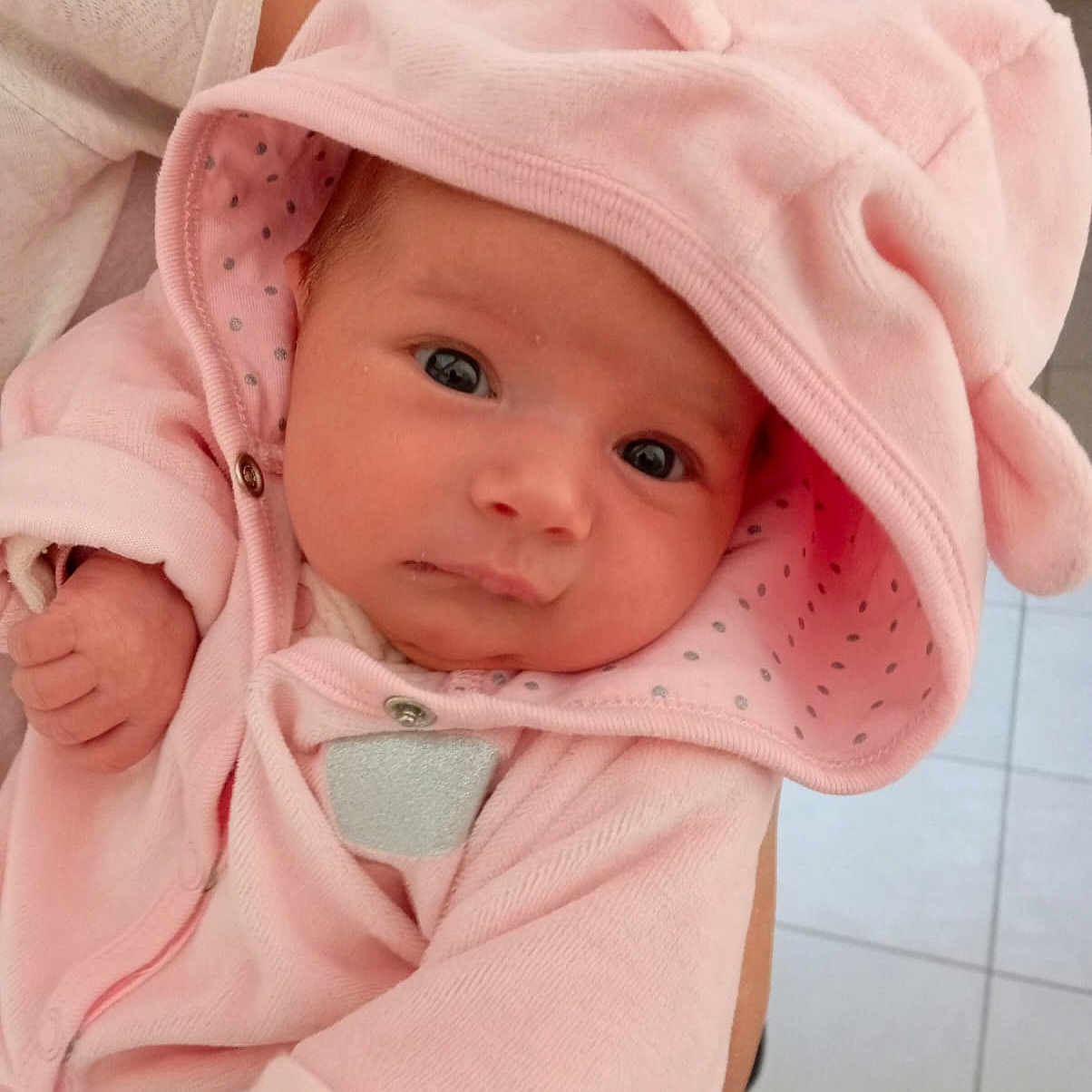Alba a rejoint le concours — aidez-le/la à gagner de superbes lots ! adorable, baby, child, closeup, cozy, cute, eyes, face, gaze, hand, hood, indoor, infant, newborn, person, pink_hoodie, portrait, soft_fabric, tile_floor, warm_clothing