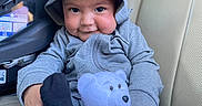 Kendrick is registered to the contest to win money with this photo: baby, beige_seat, car_interior, car_seat, child, clothing, cozy, cute, face, hand, hoodie, indoor, infant, plush, portrait, sitting, smile, teddy_bear, toy, young_child